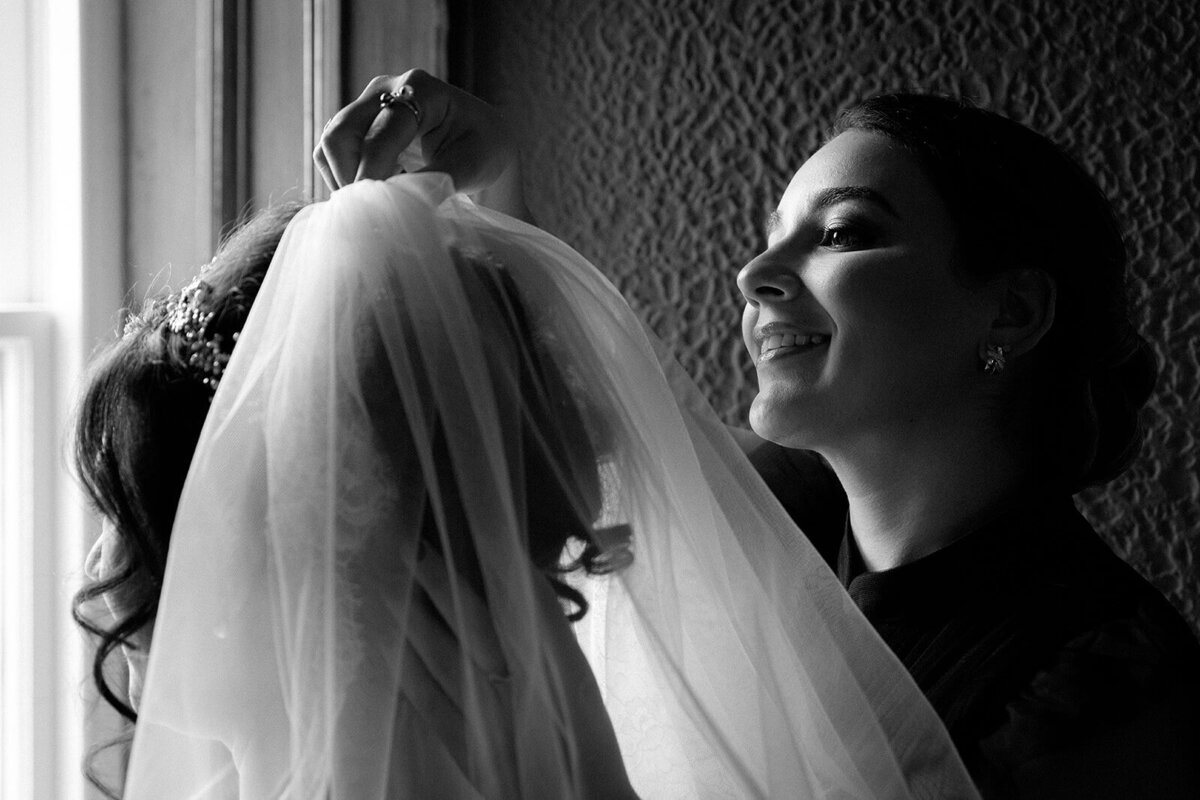 The maid of honour adjusts the brides veil in front of a window at an Edinburgh castle.