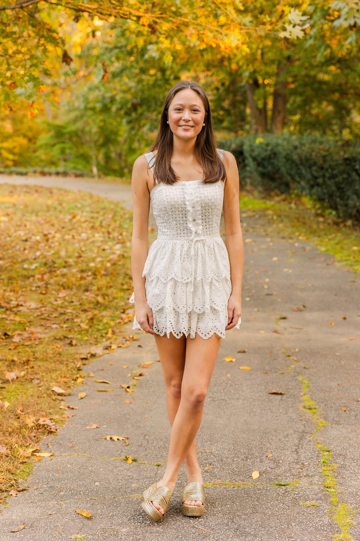 wide shot of senior girl standing ankles crosses in the middle of a park path during portrait session