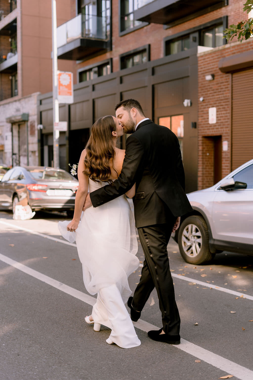 groom with his arm around bride as they walk down a street and kiss