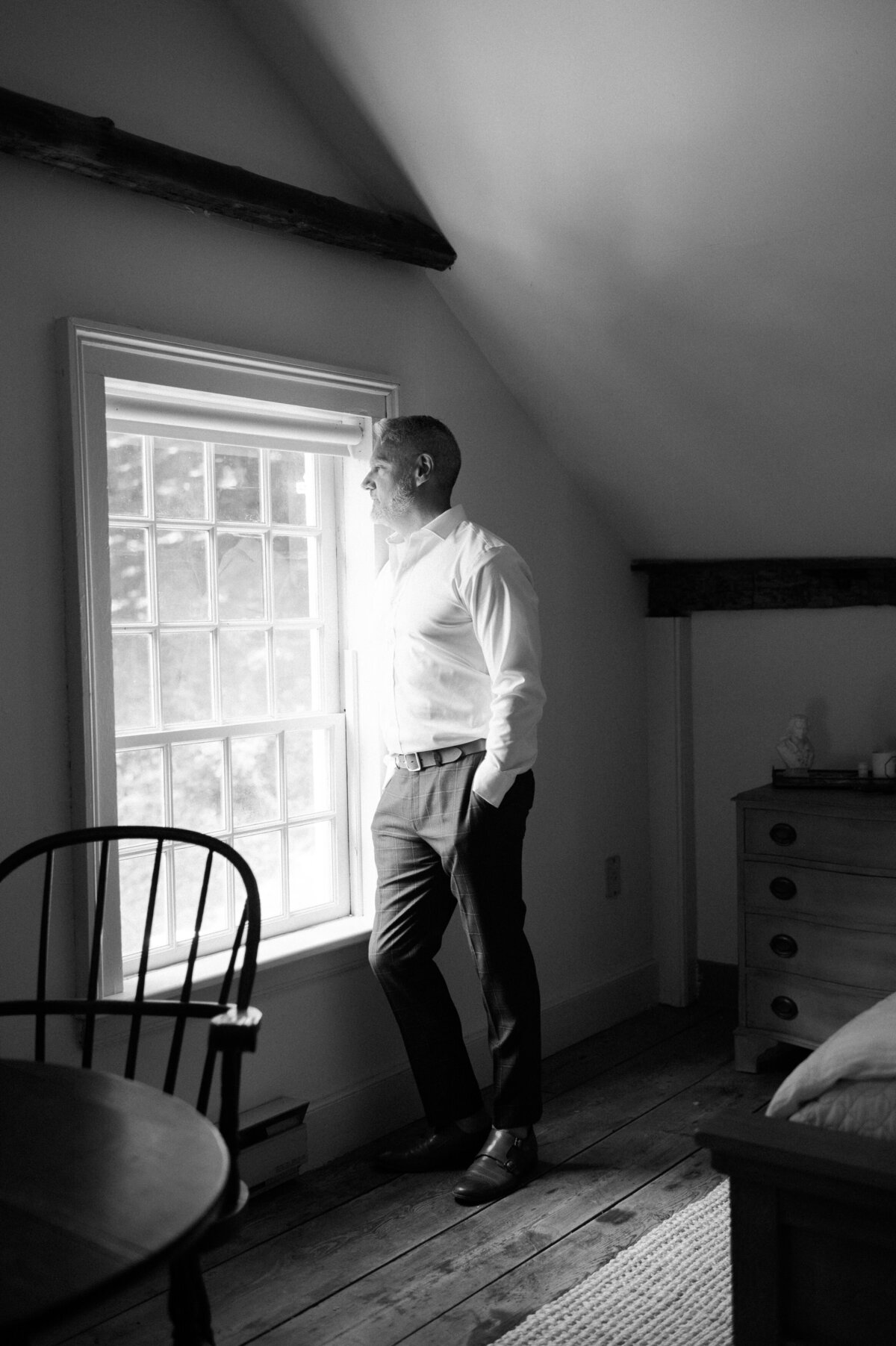 Groom leaning against a sun lit window 