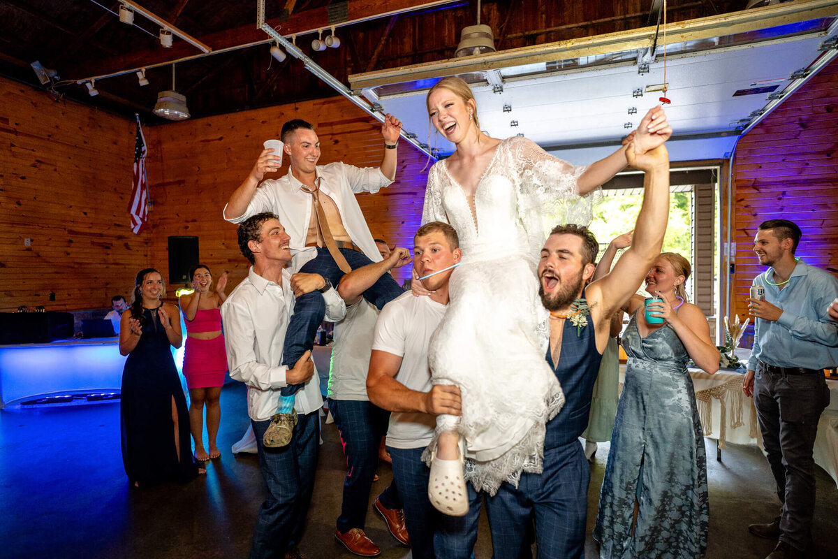 photo of wedding guests lifting bride and groom onto their shoulders and cheering during a wedding reception