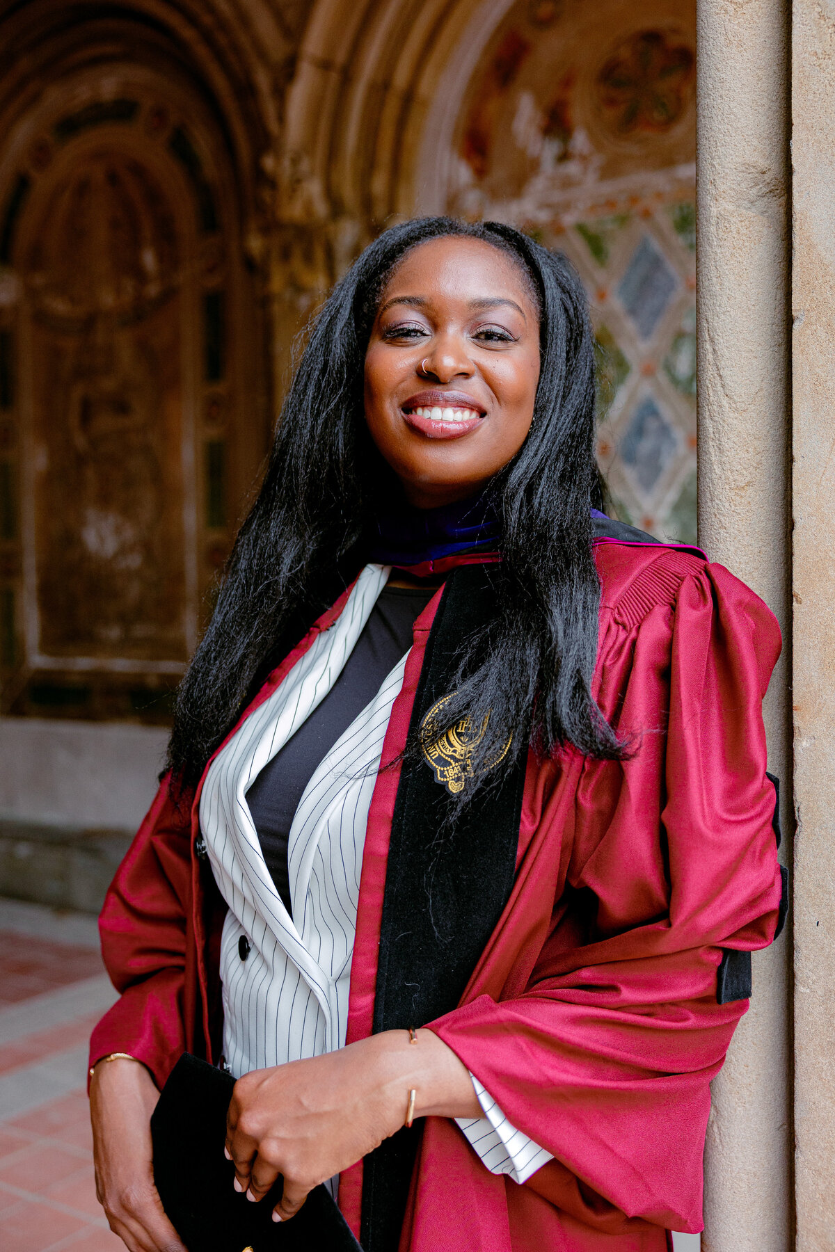 Fordham graduate smiling in red gown during portraits at Central Park.
