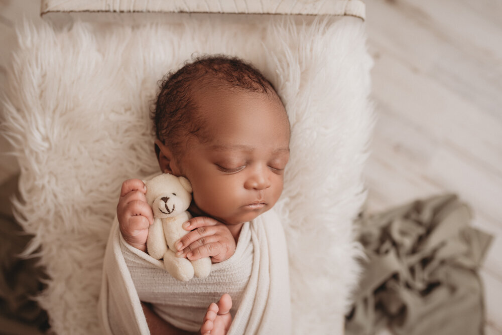 Newborn photos with Atlanta, Georgia newborn photographer of sleeping baby boy with hands under chin holding a tiny white bear and laying in little bed.