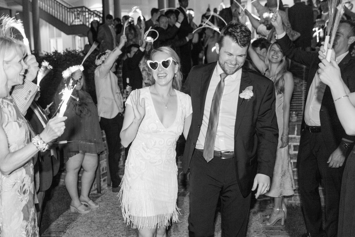 bride and groom exit reception while bride wears heart shaped sunglasses