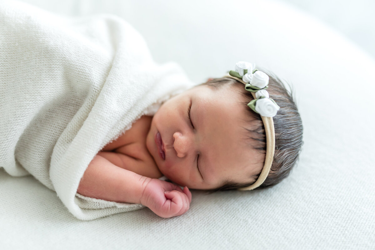 Newborn asleep with loose blanket and flowery headband