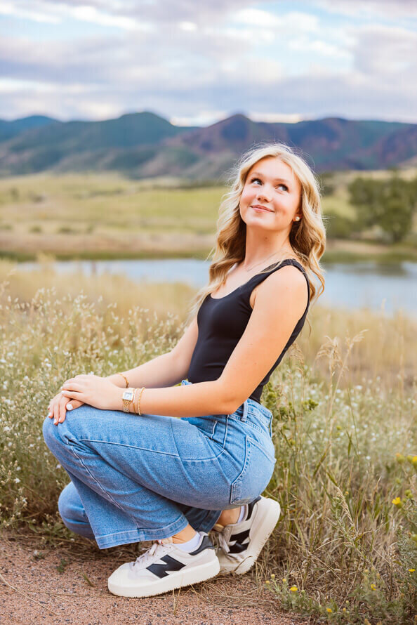 Senior girl squats and look up with mountains in the background.