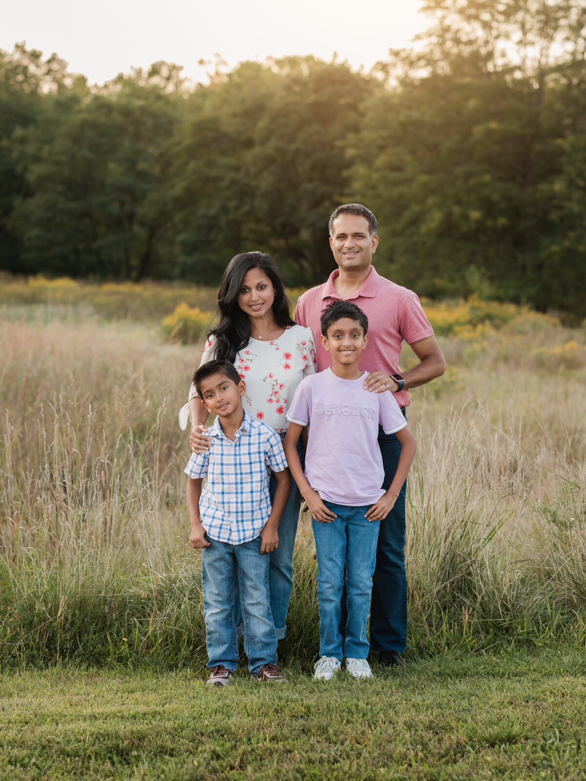 mom dad and two sons posing in field for family photos