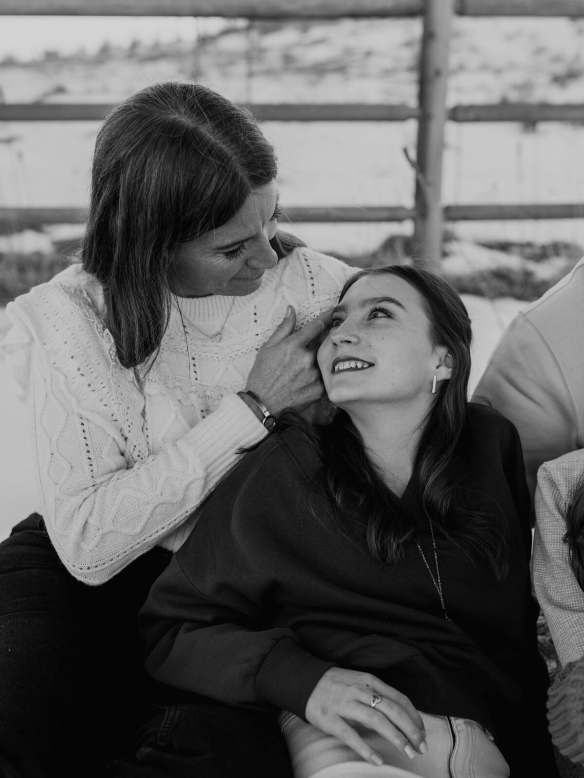 A fine art portrait of a mother and a daughter, looking at each other during an outdoor family photography session with a snowy backdrop.