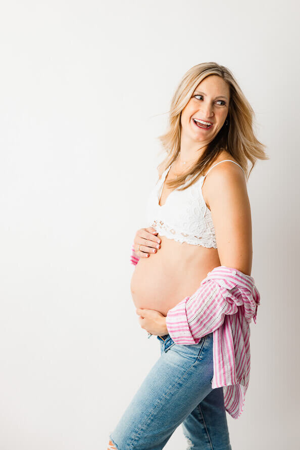 A pregnant woman with no shirt on laughs over her shoulder.
