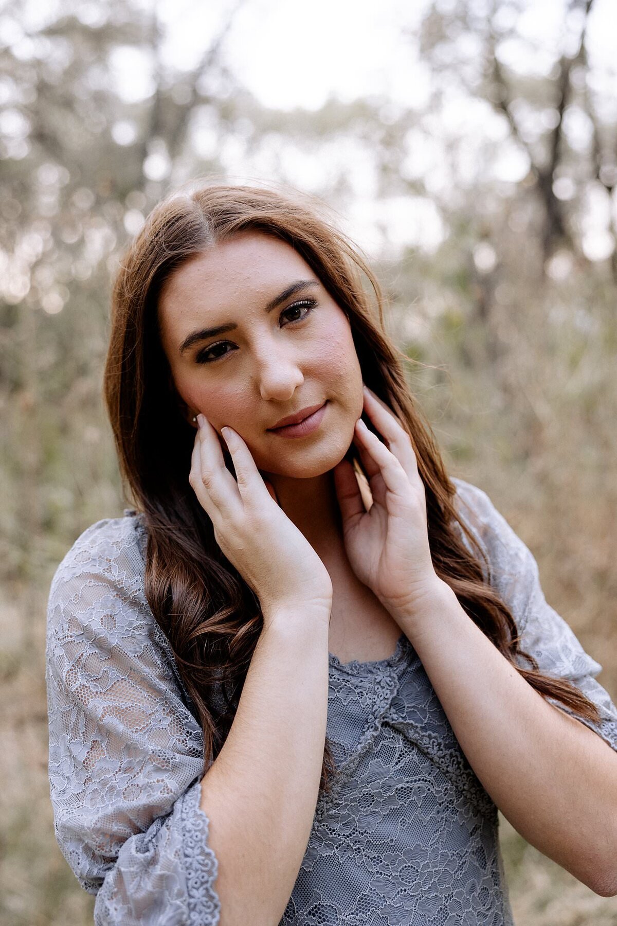 Senior girl cupping her face looking at the camera.