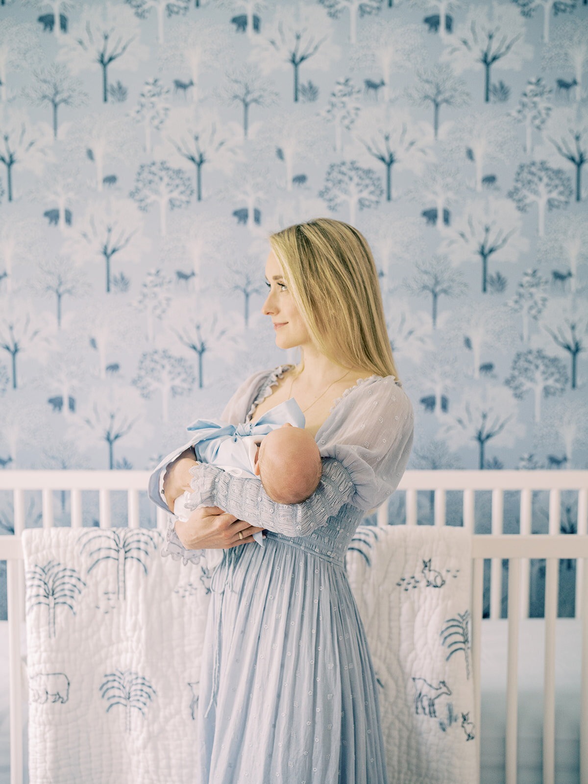 Blonde mother stands in her blue Serena & Lily nursery holding her baby boy.