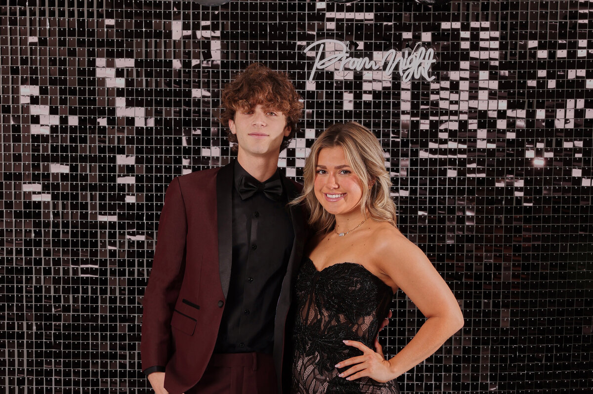 A boy holding a cake that says “Prom?” while wearing his black prom suit