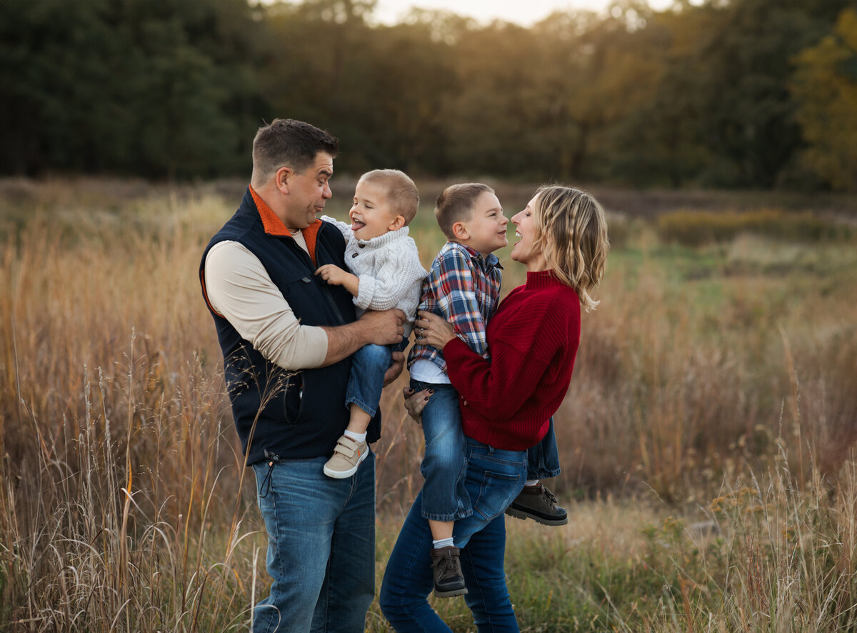 mom dad and two sons posed in field for family photoshoot 