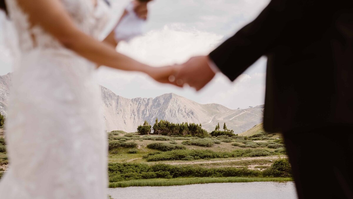 Bride and groom hold hands with mountain views in the background during their wedding vows in Colorado.