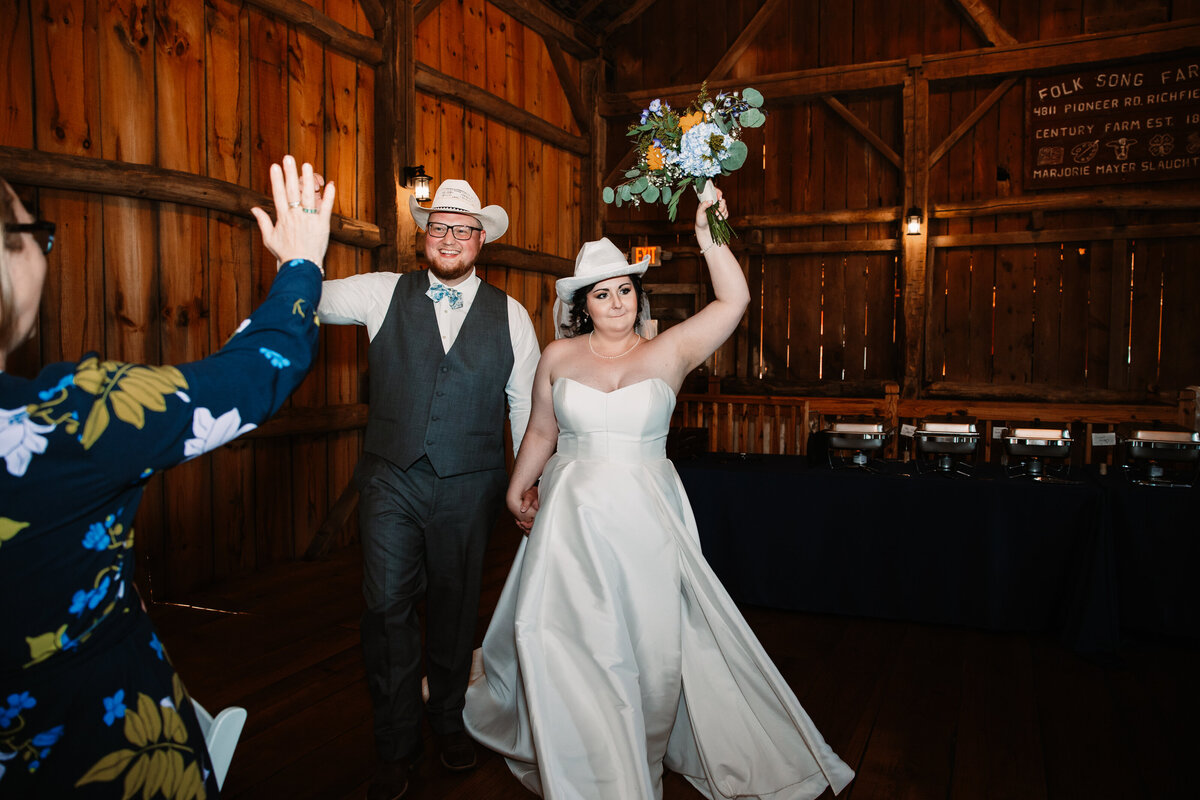 Newlyweds enter their reception to cheers while wearing white cowboy hats
