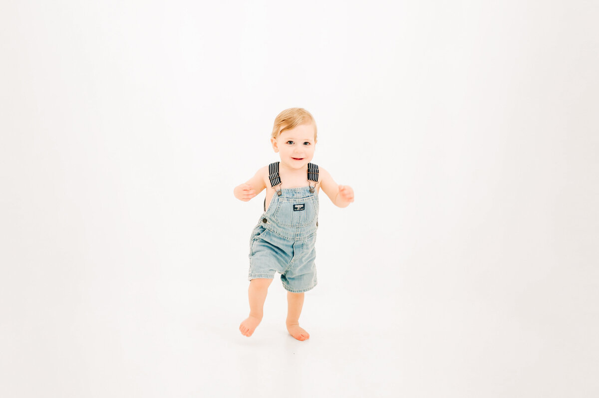 toddler boy walking in white photography studio during Springfield MO 1st birthday photography session