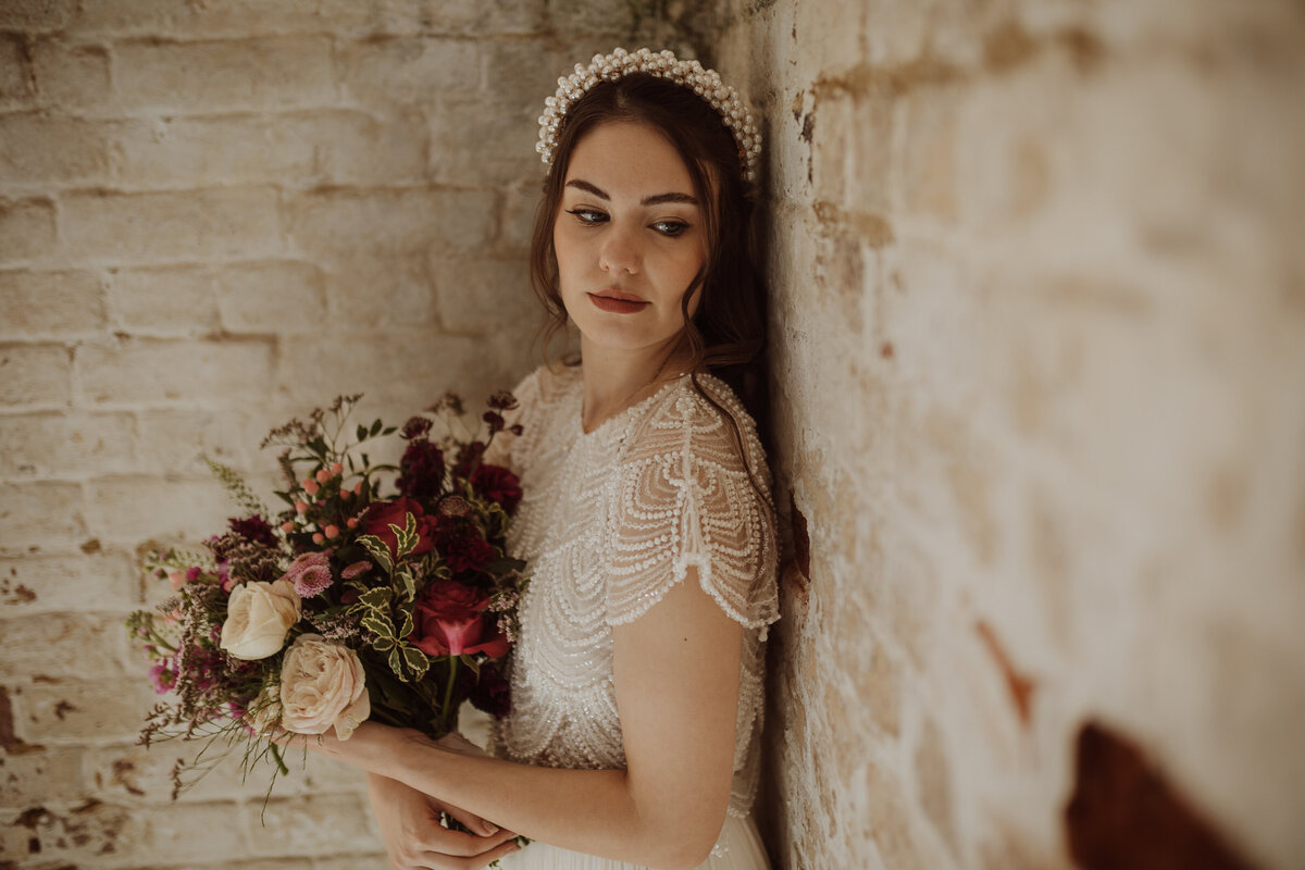 Bride standing near a wall with a bouquet of flowers