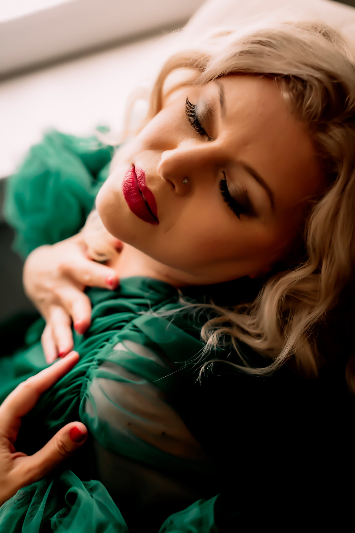 closeup of a blonde haired woman with eyes closed and hands on her chest while wearing a green robe