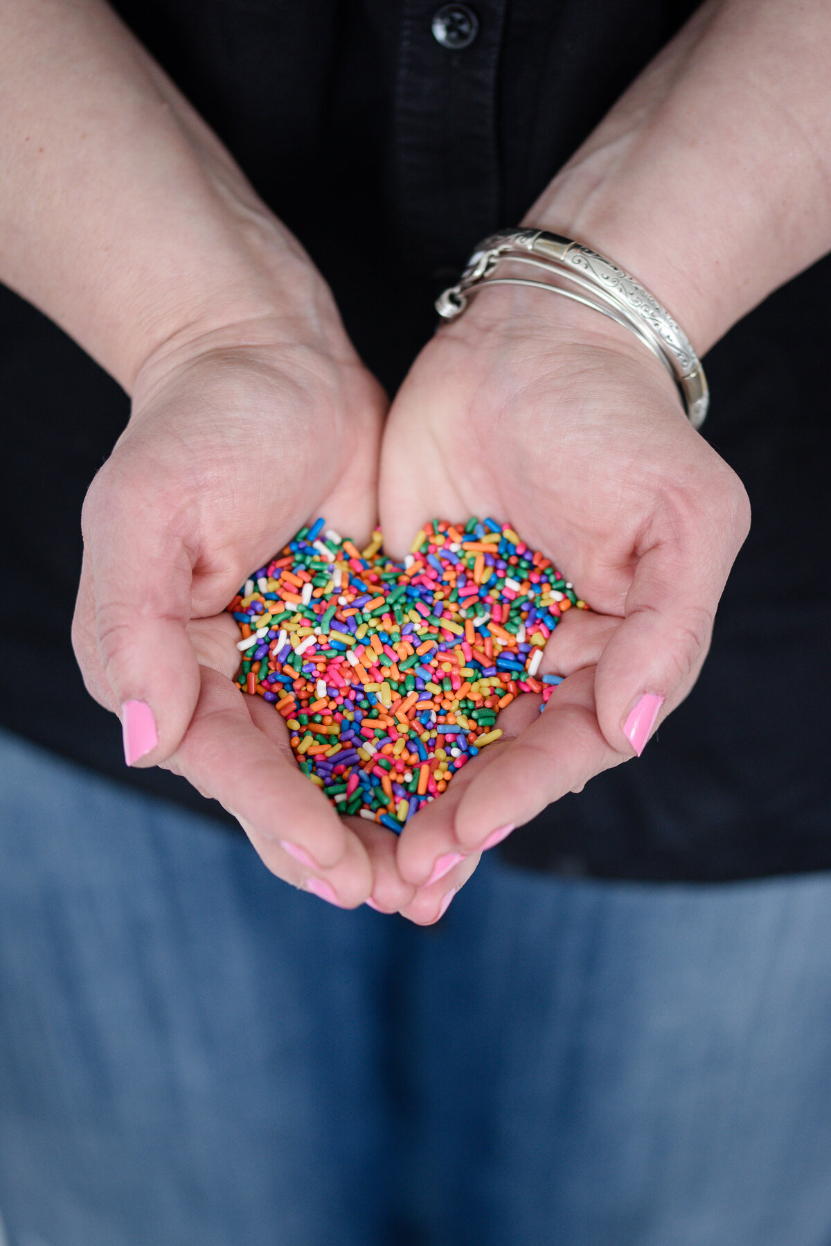 a woman with pink fingernails holds her hands out and in the hands are colored sprinkles in the shape of a heart as taken by a branding photographer near me