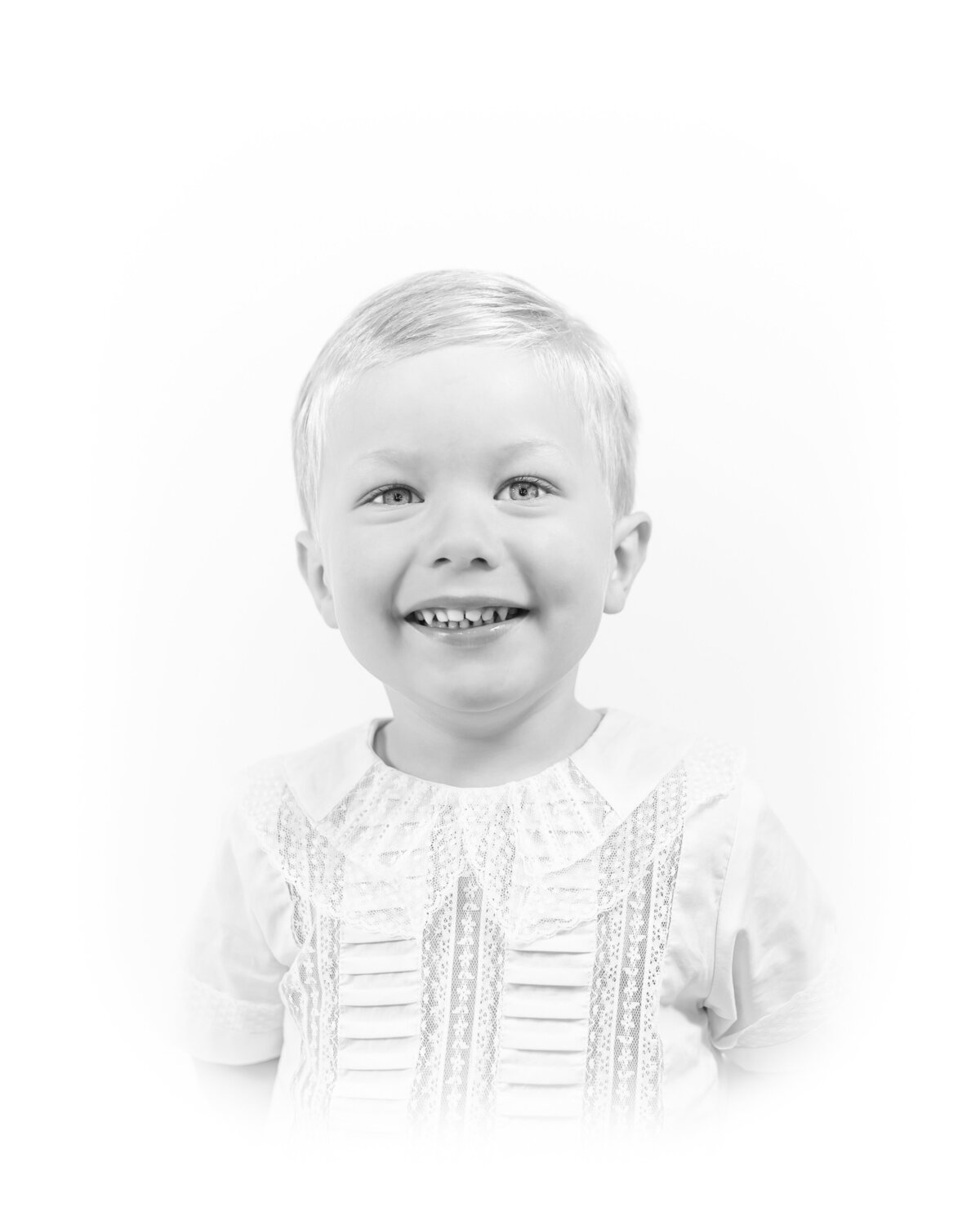 Black and white heirloom portrait of a smiling baby dressed in a classic white outfit with lace details. This timeless baby photography captures the innocence and joy of childhood, created by a Birmingham newborn photographer specializing in elegant, light-filled portraits.