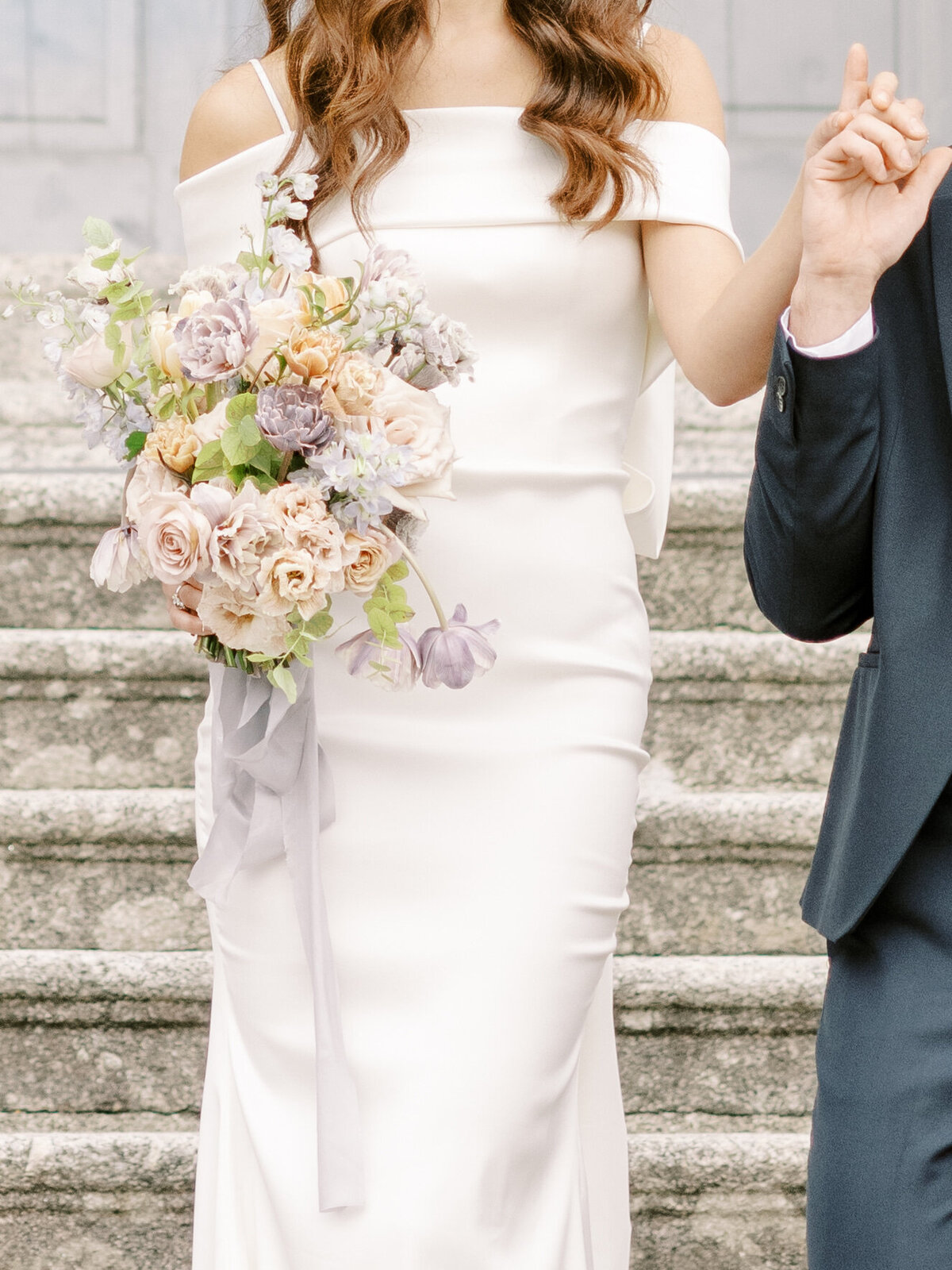 Bride and groom with bride holding a blush pink and purple wedding bouquet during their Villa Sola Cabiati wedding on Lake Como in Italy photographed by Bride and groom in an intimate moment on the balcony of Villa Sola Cabiati on Lake Como bride in an off the shoulder wedding dress with oversized bow in the back and groom in navy suit during their Lake Como wedding photographed by Italy wedding photographer