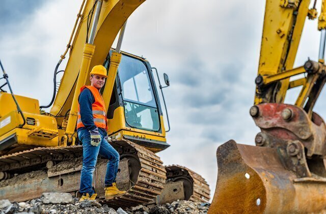 Construction worker standing in front of an excavator