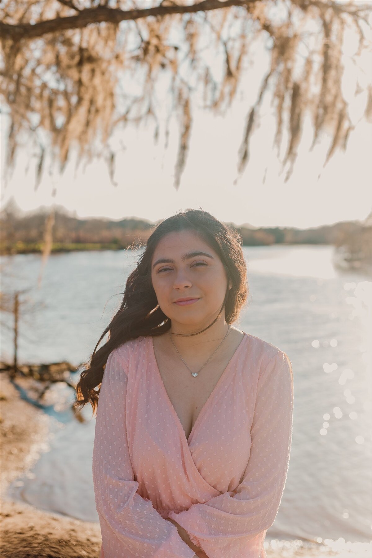 young girl celebrating her 16th birthday with a portrait session at Walter Hall Park in League City, Texas, wearing a light pink dress with a serene lake backdrop and soft natural lighting.