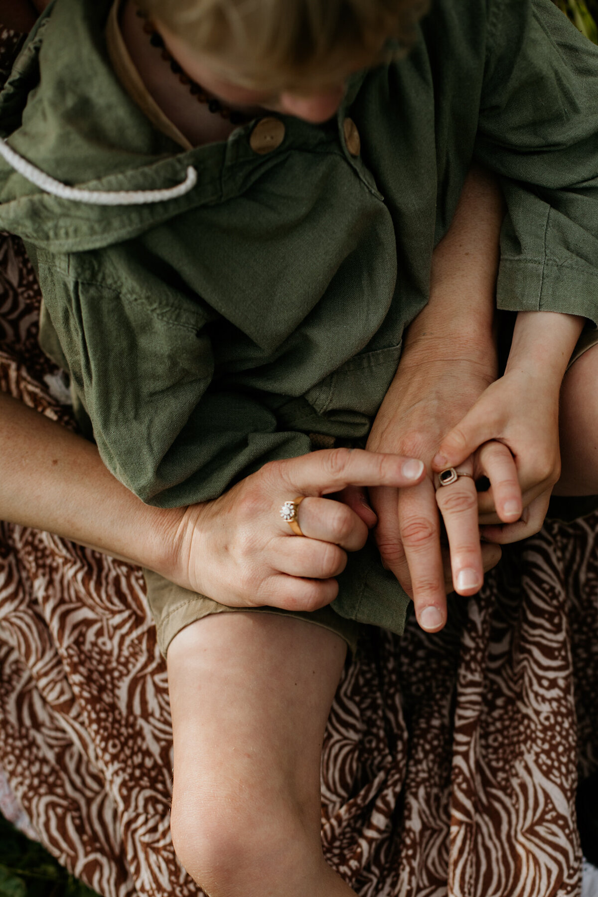 Close-up of a child’s head in his mom’s hands, highlighting her rings.