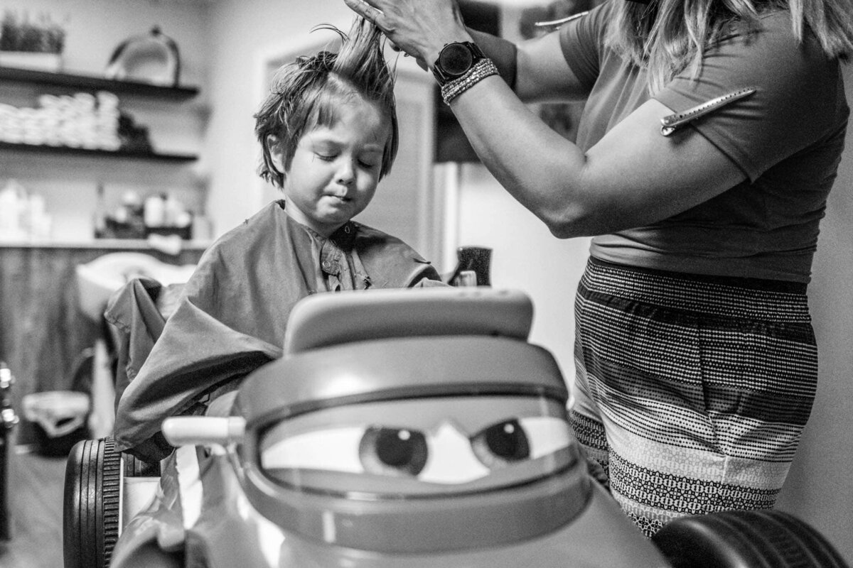 A boy gets his hair cut in a race car barber's chair