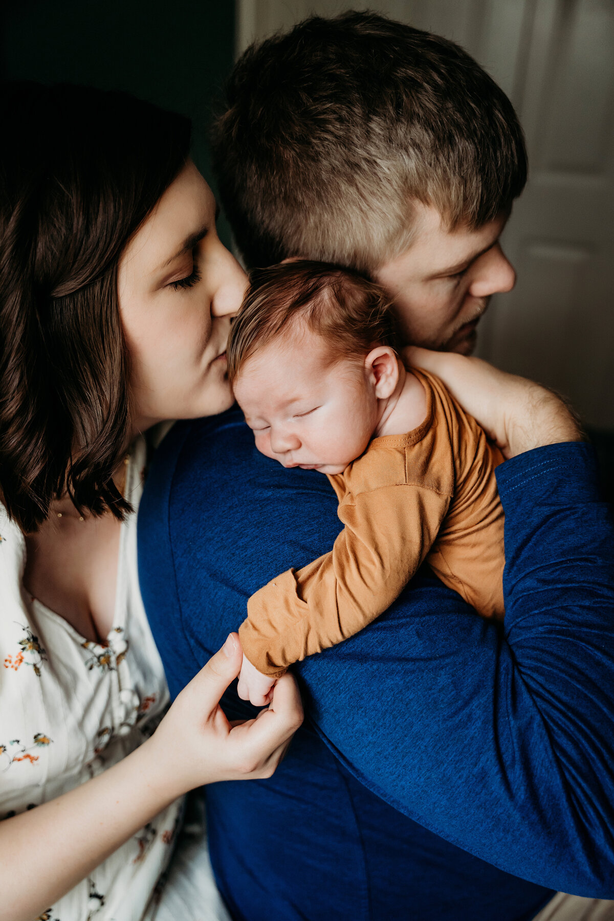 Newborn Photographer, a young dad holds baby on his shoulder and mom tenderly kisses  her little baby boy