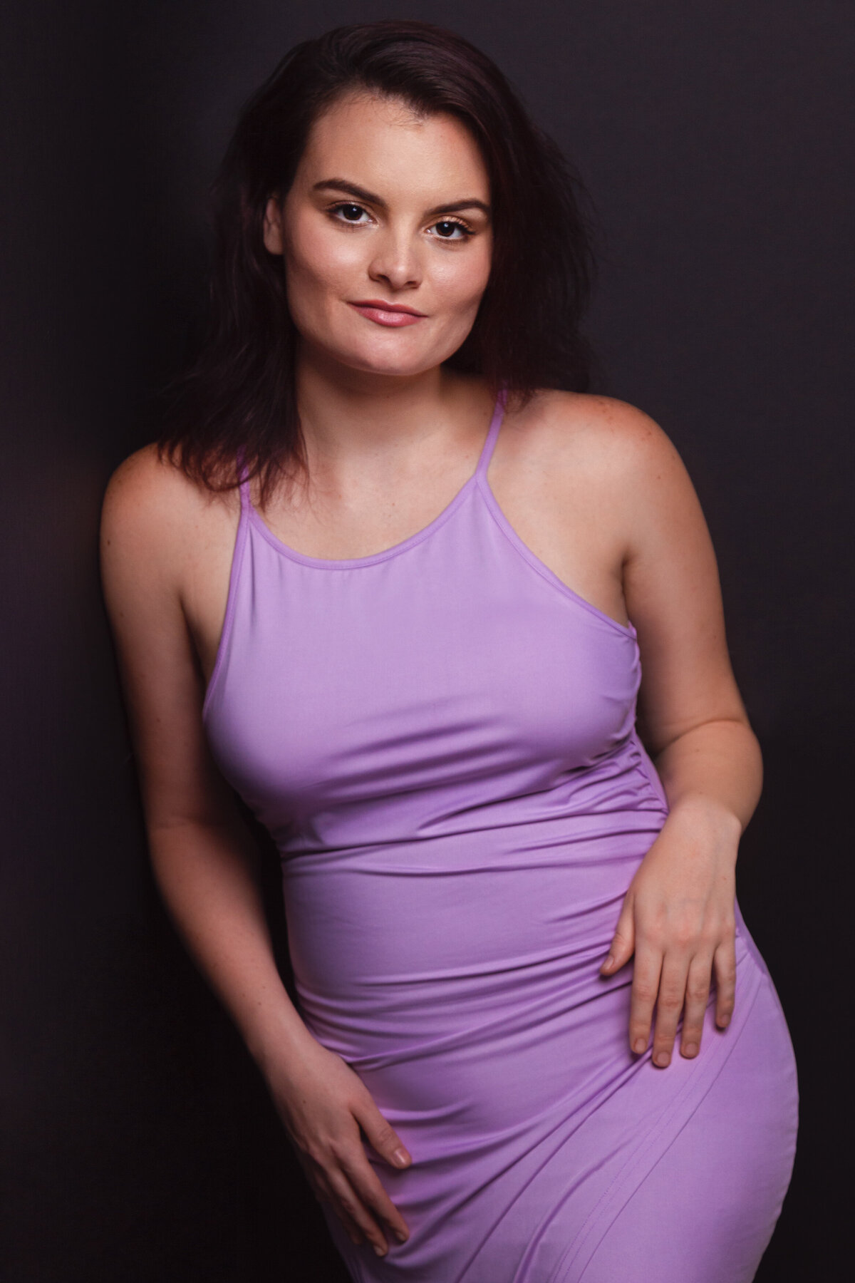 lady in purpled dress leaning on her right in a studio