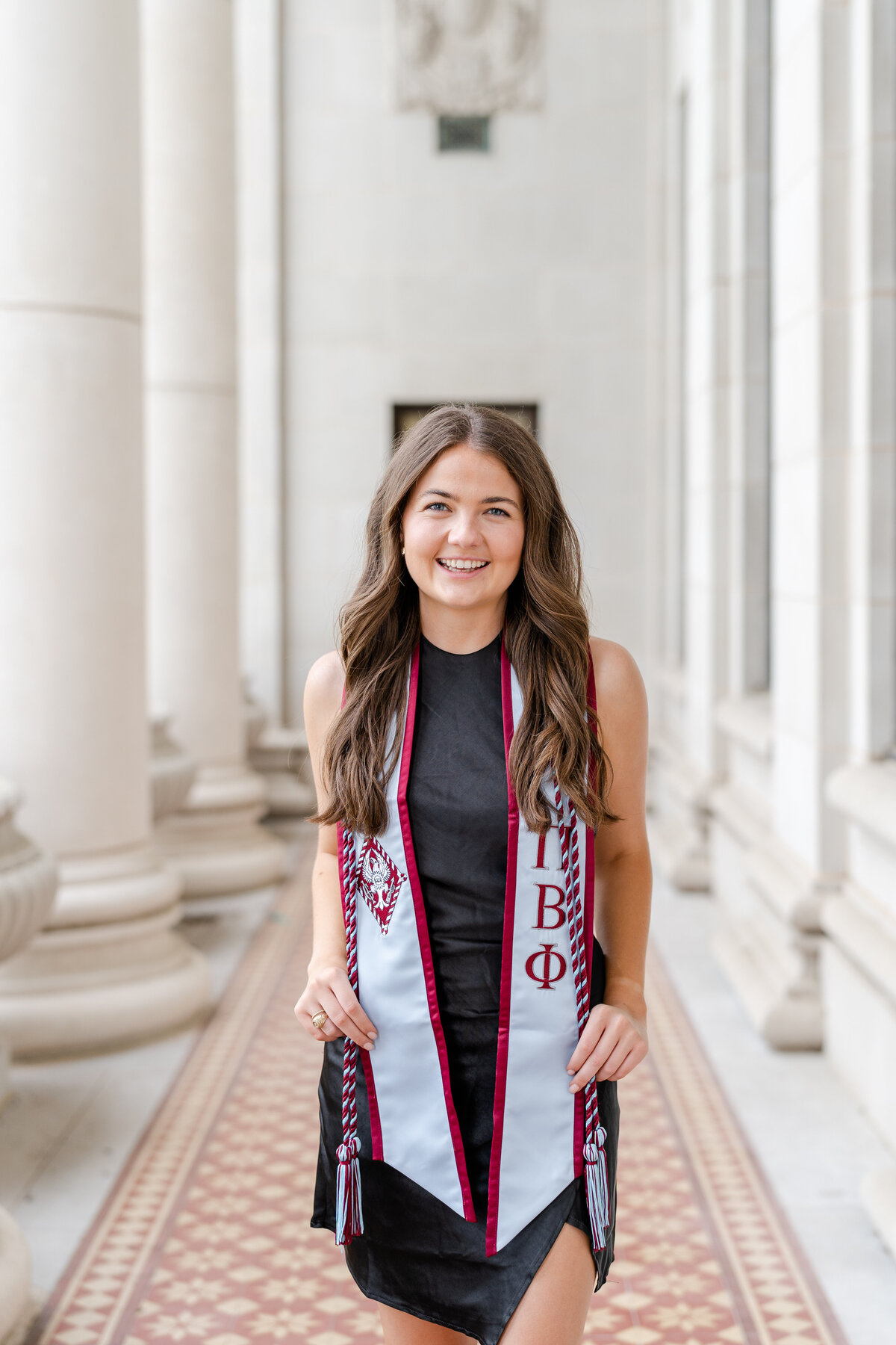 Texas A&M senior girl smiling with Pi Phi sorority stole and cords on and a black dress in the Administration Building columns
