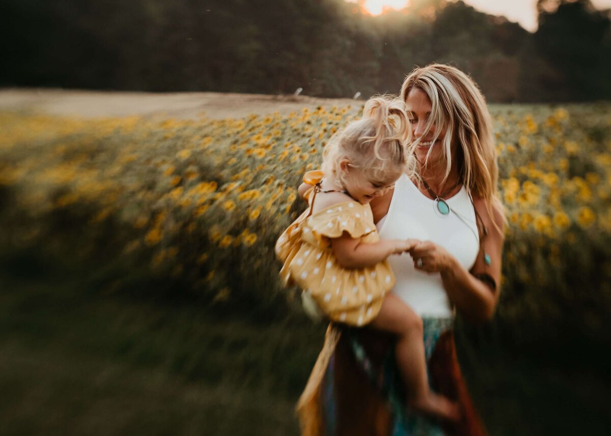 A woman holding her daughter in a field of sunflowers captured by a Pittsburgh family photographer.