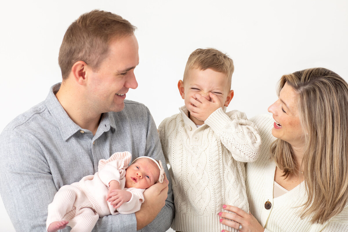 a family of four with their newborn and older son who is laughing.