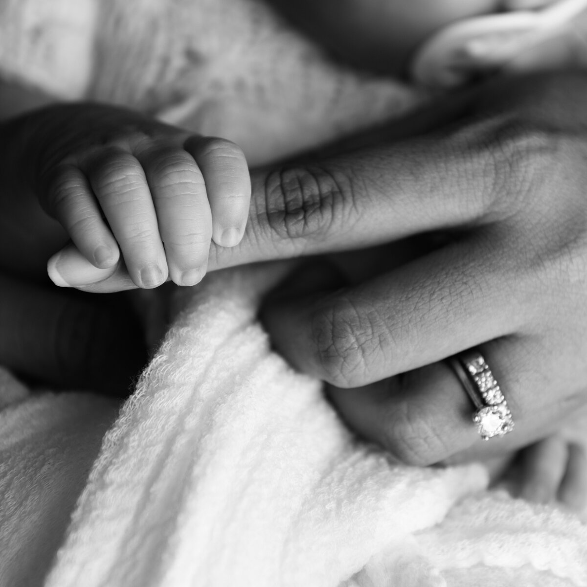 A delicate black and white macro photo of a newborn grasping mama’s finger — showcasing love in its purest form