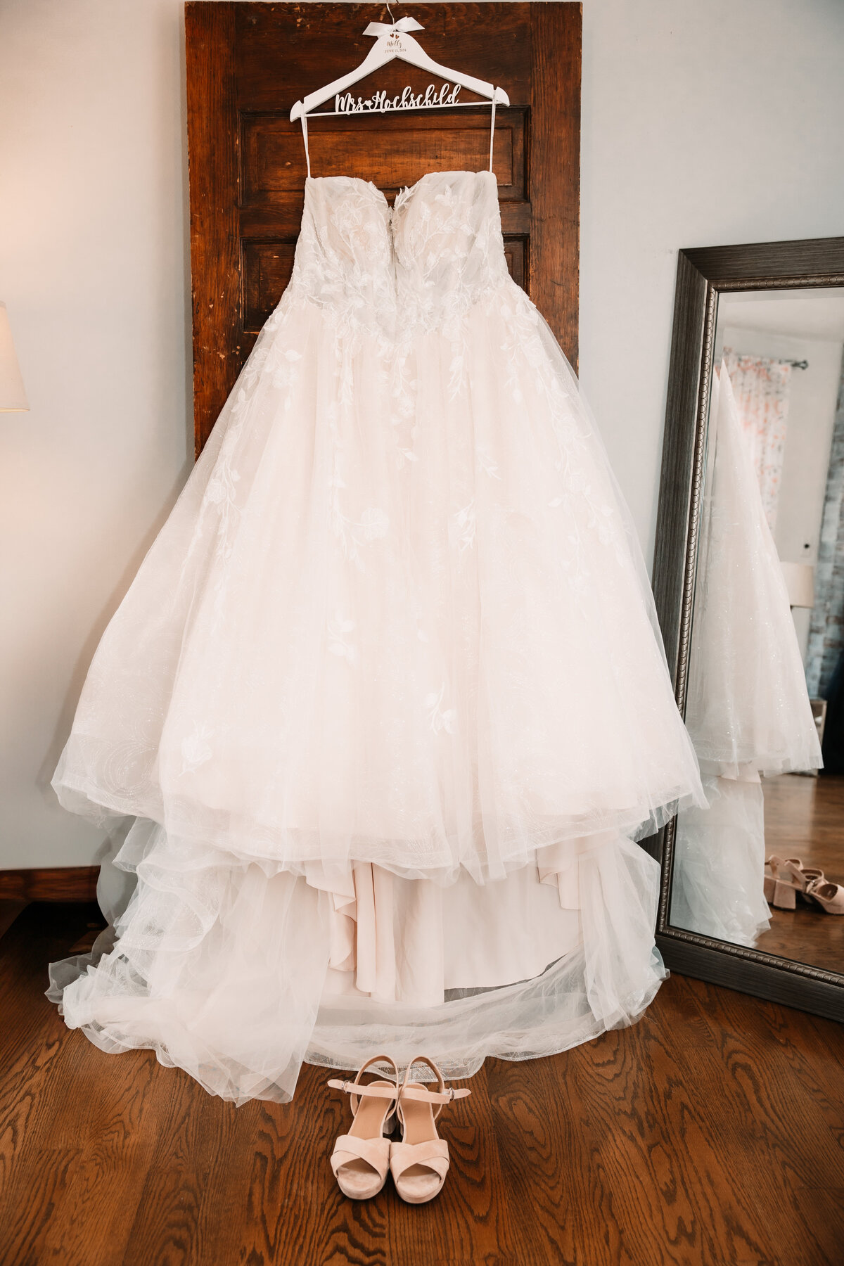 A bride's dress hangs in a doorway with shoes and custom hanger