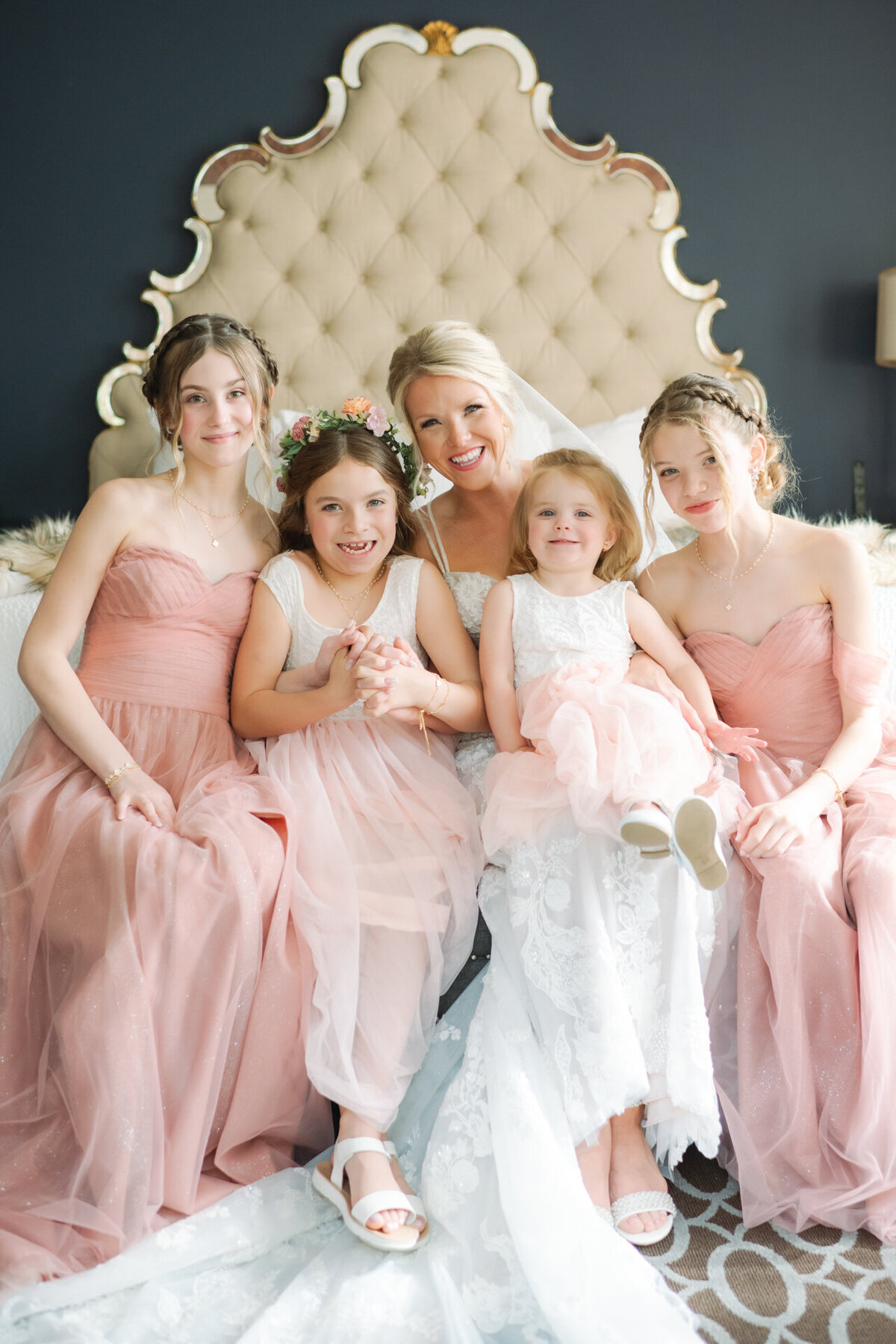 bride and flower girls smile while sitting on a bed