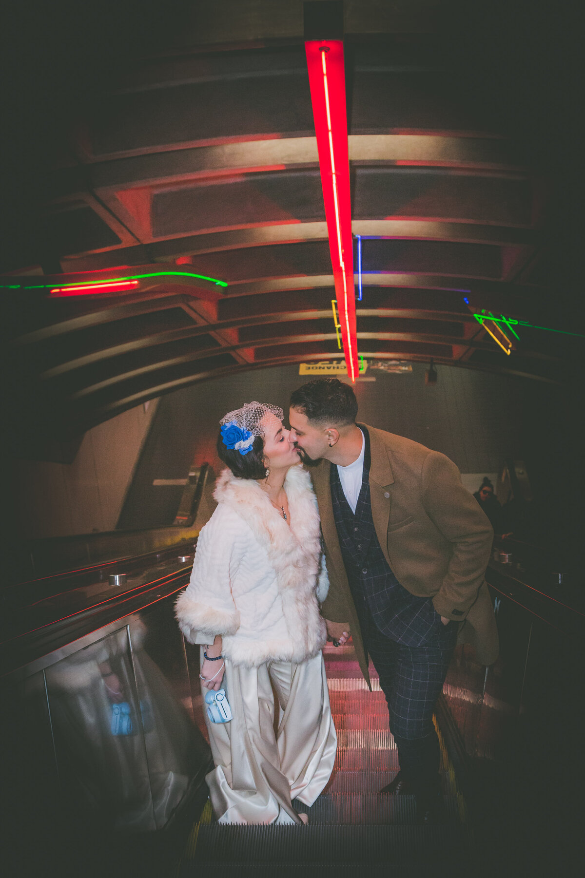 Couple kisses on escalator with cool lighting.