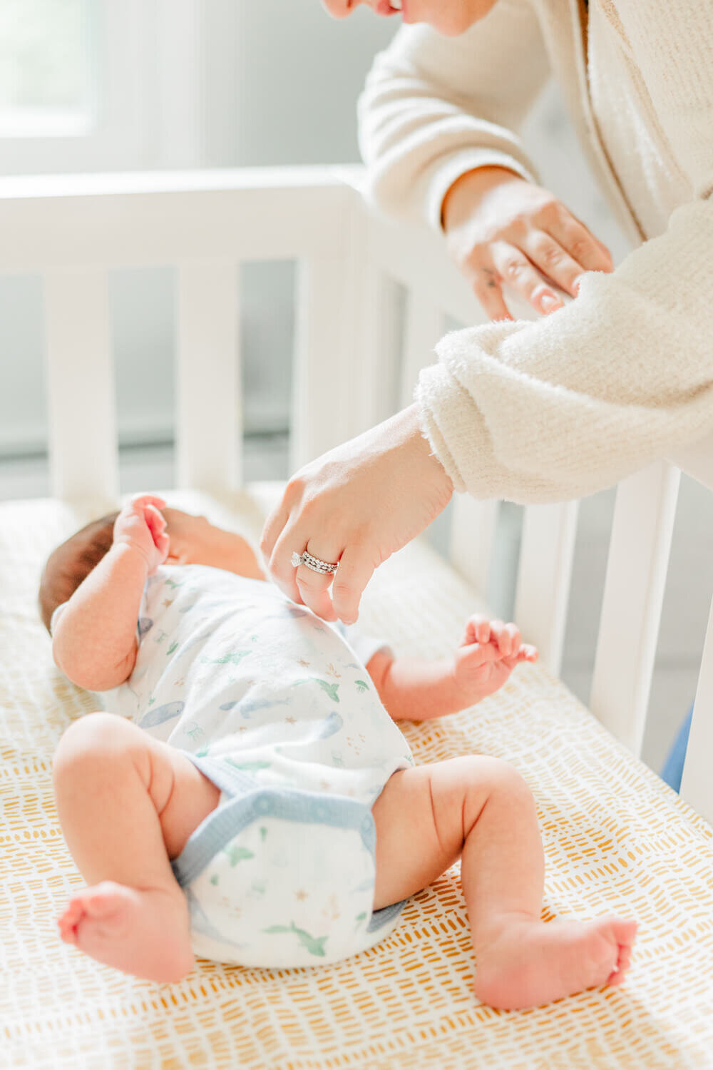 Mom leans over the side of the crib to touch her baby