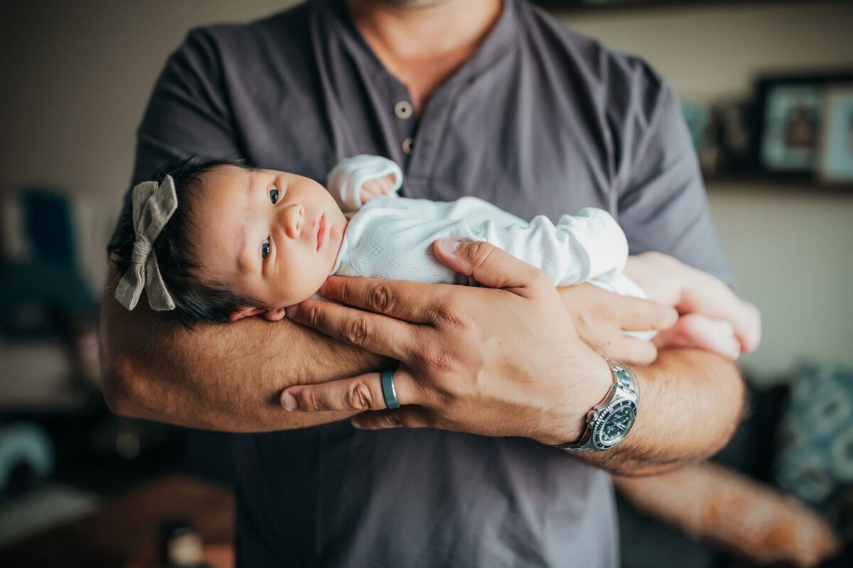 newborn dad holding newborn girl in minimalist white onesie in living room by Orange County photographer Francesca Marchese