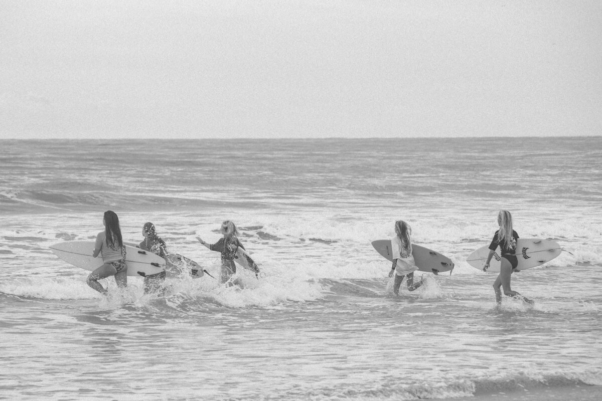 A group of surfers run into the waves while holding their shortboards