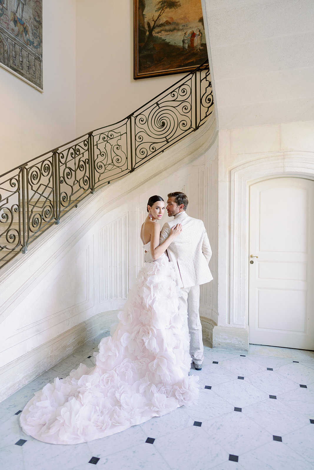 Bride and groom standing together on marble staircase with ornate wrought-iron railing at Château de Tourreau.