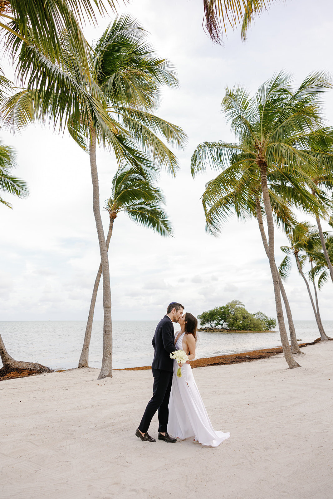 A romantic newlywed moment with the ocean and lush palm trees as the backdrop. Destination wedding photography by Claudia Amalia.