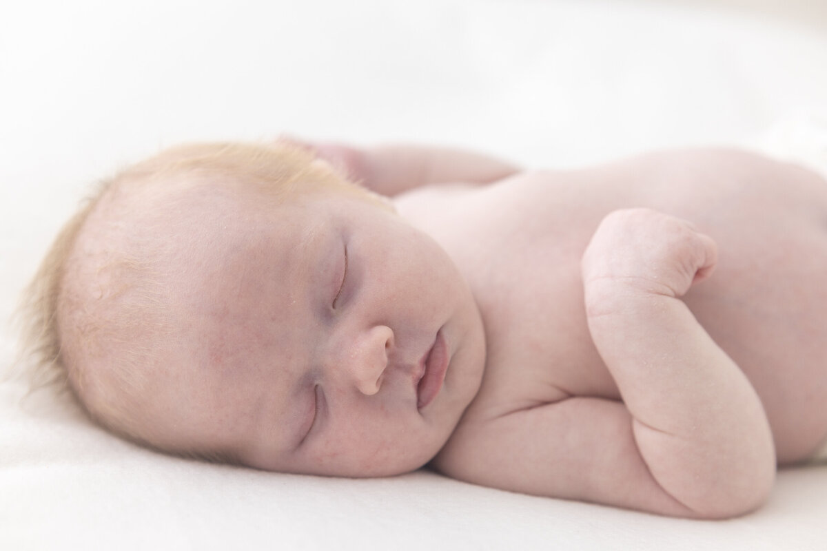 Portrettbilde av en sovende baby som ligger på et hvitt teppe, ansiktet vendt mot kamera. Fotografert i Studio Landmark, Fyllingsdalen.