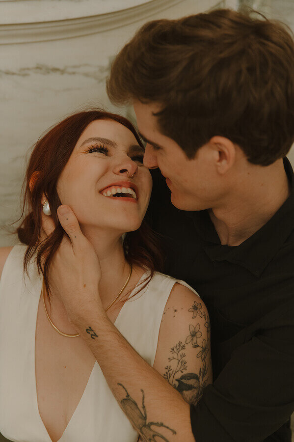 Close up if a man gently holding his fiancé's face on their elopement day. She's looking up at him laughing.