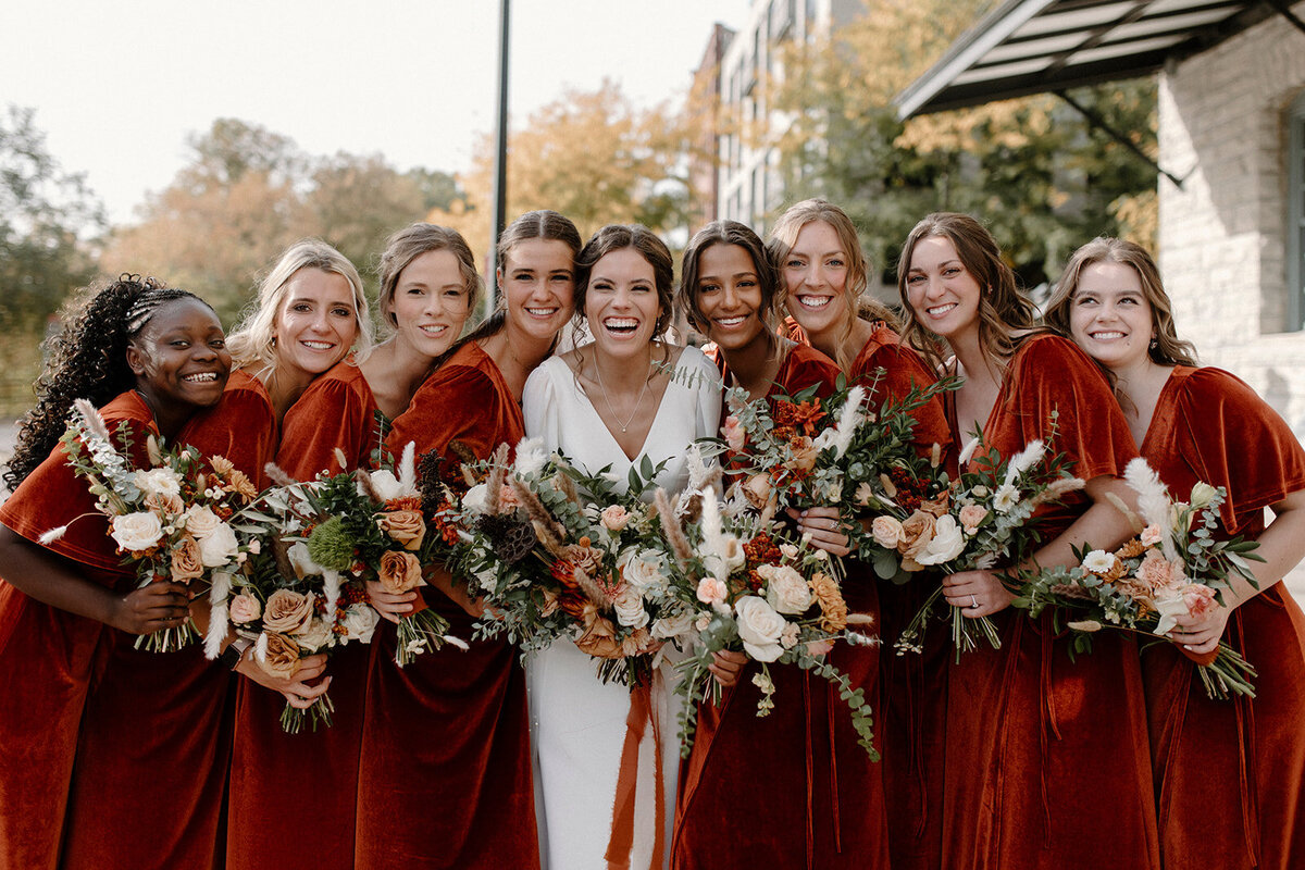 bride and bridesmaids holding bouquets of orange and red flowers