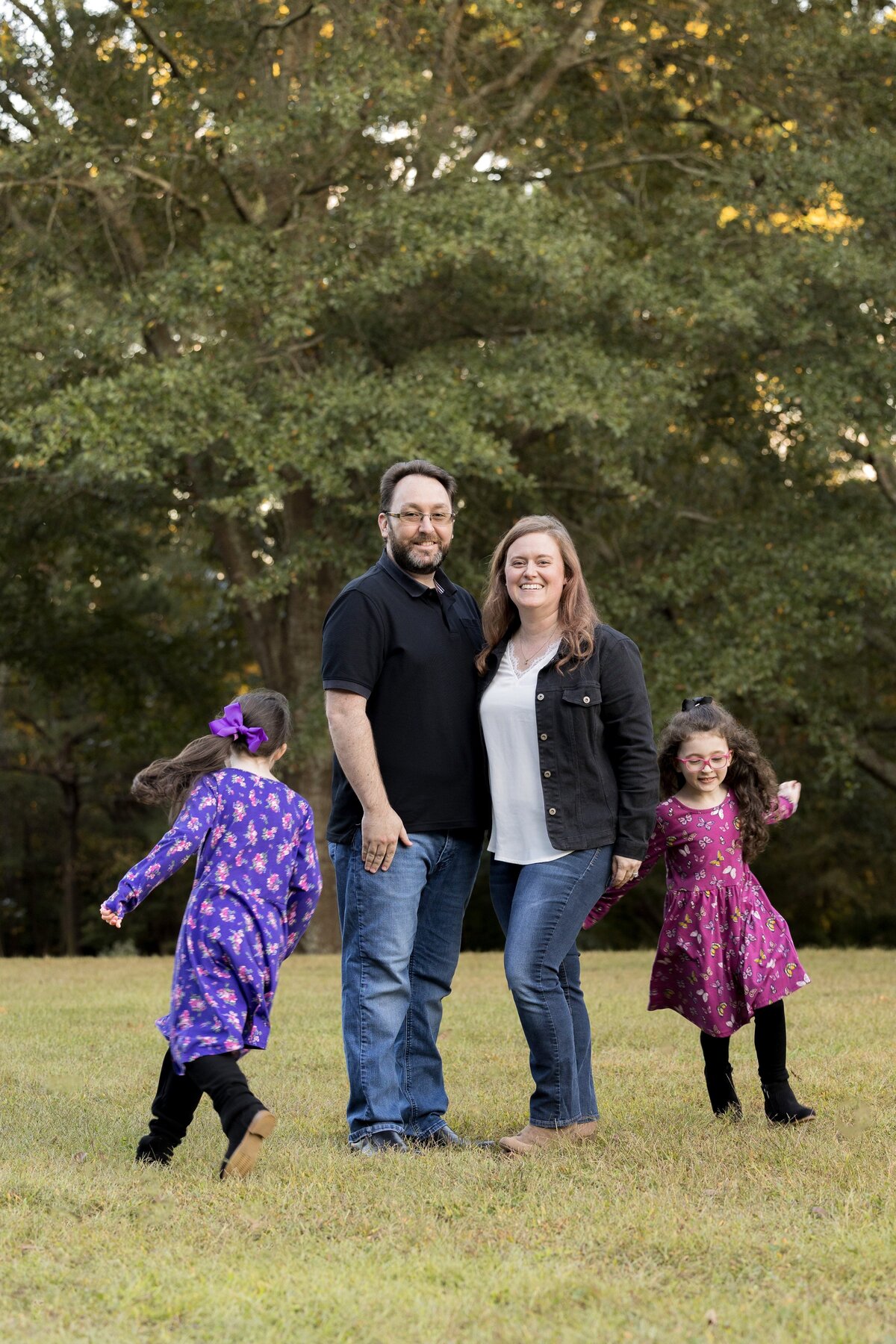 a mom and dad standing in a field with two children running