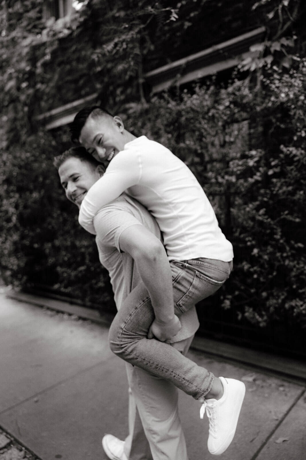 The engaged man is carrying his fiancé in front of an ivy-covered building in West Village, NYC. Image by Jenny Fu Studio