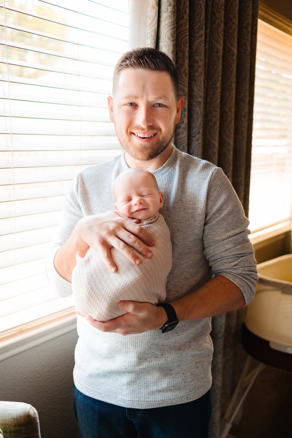 the best maternity photographer in Albuquerque with this touching image of a dad with his beautiful baby. The father is dressed in blue pants and a grey sweater, while the baby is wrapped in a cozy white blanket.