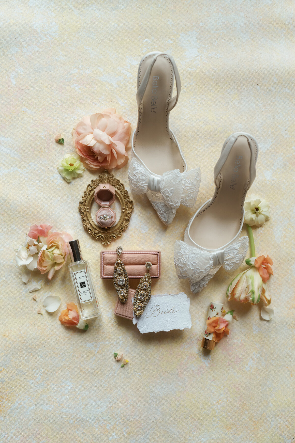 Flat lay of wedding details including shoes, perfumes and jewelry.